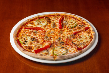 Italian pizza with cheese and vegetables on a plate on a wooden background