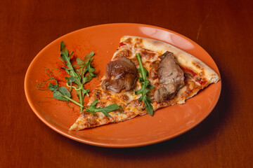 Slice of Italian pizza with roast beef on a plate on a wooden background