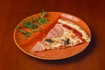 Slice of Italian pizza with ham and mushrooms on a plate on a wooden background