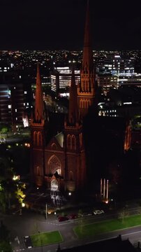 Vertical drone shot circling the Saint Patrick&acute;s cathedral, night in Melbourne