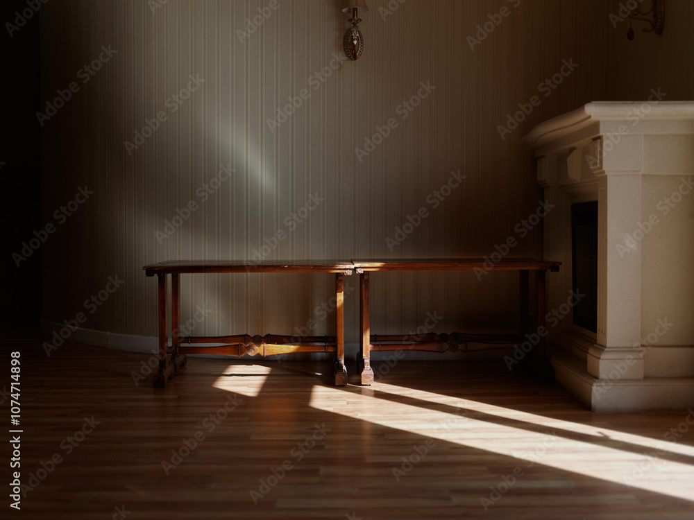 Poster an empty wooden table standing in a dimly lit room with soft shadows and warm sunlight streaming thr