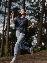 Energetic young woman jogging in a forest, surrounded by tall trees, dressed in comfortable athletic wear, expressing joy and enthusiasm Nature and fitness concept