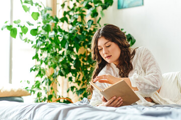 A beautiful young plus size woman relaxes while reading a book in her cozy home setting.