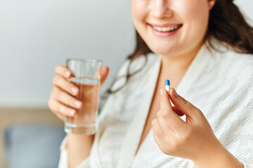 A joyful plus size woman holds a glass of water and a pill, embracing her wellness routine.