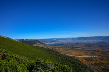 Scenic overlook of a vast valley with colorful autumn foliage, evergreen trees, and a clear blue sky