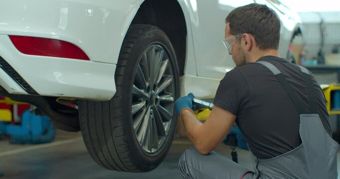 Mechanic is unscrewing lug nuts with a pneumatic impact wrench. Specialists removes the wheel in order to fix a component on a vehicle.