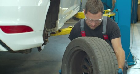Mechanic is unscrewing lug nuts with a pneumatic impact wrench. Specialists removes the wheel in order to fix a component on a vehicle.