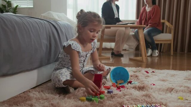 Wide shot of small girl playing with toys while her mother talking with social worker in background at home