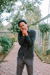 Southeast Asian man holding his cheek with a pained expression, indicating a toothache.