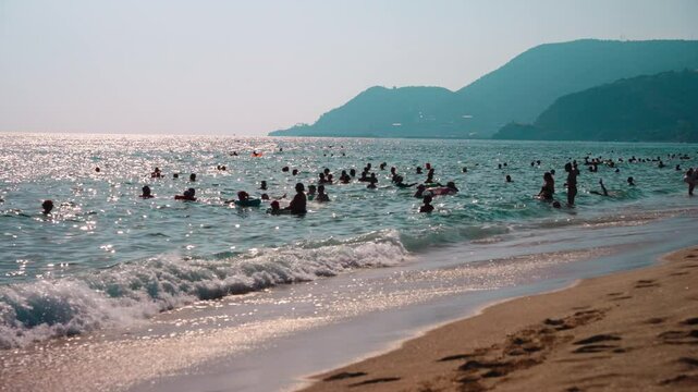 Lots of people on the beach during the summer season. The popular sandy Cleopatra Beach in Turkey. Silhouettes of people on the background of the sea, beach, and mountains. Summer season