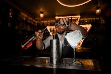 Metal mixing glass and a martini glass filled with crushed ice for a cocktail are on the bar