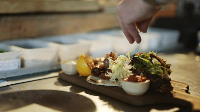 Beautiful dish with grilled meat and vegetables on a wooden fancy designer plate on a wooden kitchen surface and hands of a person garnishing it