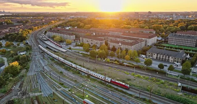 Aerial drone view of a train moving on the tracks near Vesterbro district in Copenhagen, Denmark at sunset