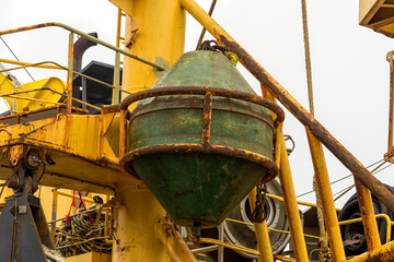 green rusty boiler hanging from a yellow steel structure aboard a stern trawler