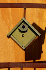 Close-Up of Birdhouse Hanging on Rusty Metal Fence with Shadow on Wall