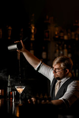 Male bartender with a serious expression pours the last drops of a cocktail into a glass