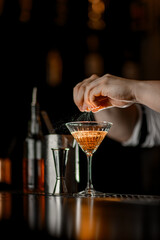 Male hands hold a piece of orange peel over a glass with a cocktail, and squeeze it