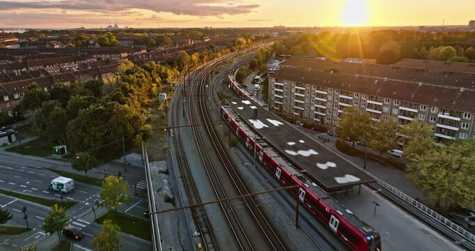 Aerial drone view of a train moving on the tracks near Vesterbro district in Copenhagen, Denmark at sunset