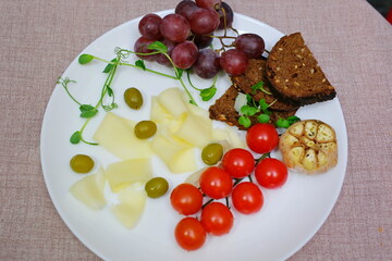 sprinkle black pepper cheese on a white plate olives grapes cherry tomatoes delicious fresh cheese and sprouts of sprouted greens. microgreens