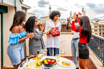 Friends applauding while man receiving birthday gift during rooftop party