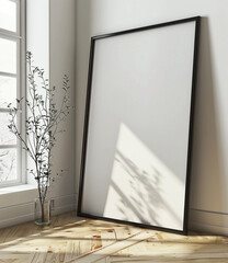 a black framed poster mockup leaning against the wall on wooden floor with window reflections