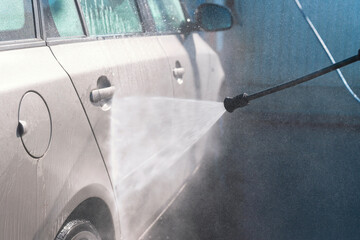 Cleaning a car using a high-pressure washer in a car wash during a sunny day with water spraying...