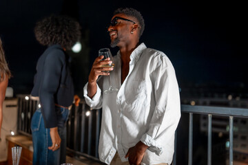 Brunette man laughing drinking alcohol at night party at terrace