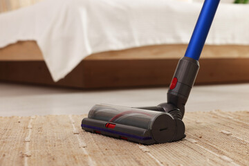 Cleaning rug with cordless vacuum cleaner indoors, closeup