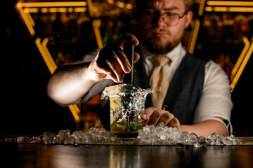 Focus on a glass of lemon cocktail, which the bartender stirs with a bar mixer so that the liquid rises above the glass