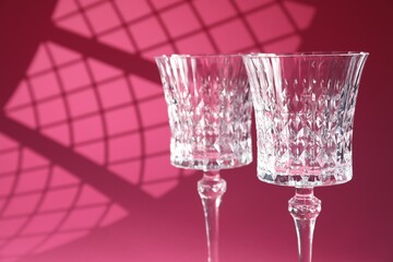 Elegant wine glasses on pink background, space for text