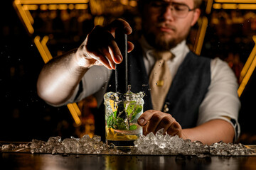 Close up of a glass of lemon cocktail with mint leaves, which the bartender mixes with a small mixer