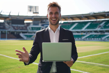 Smiling businessman with laptop giving thumbs up at a soccer stadium.