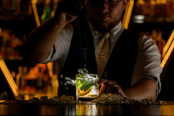 Bartender has mixed a delicious cocktail with lemon wedges and mint leaves with a portable mixer