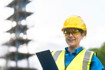 Construction worker smiling at a building site while holding a clipboard during daytime work