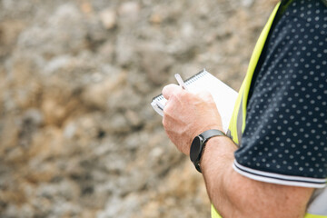 Construction site manadger taking notes while assessing site conditions and progress of planned...