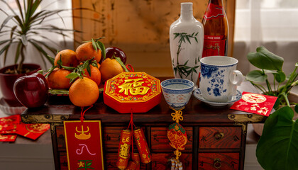A bottle of wine and cups. A plate of fruits and good fortune Chinese New Year decorations, and red packets on a traditional wooden chest. A Lunar New Year concept, background.