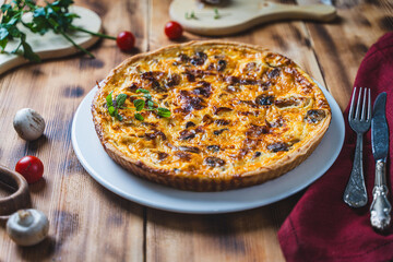 Quiche or pie with meat, chicken and mushrooms on a wooden table with cutlery, herbs and cherry tomatoes