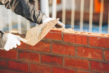 A skilled worker uses a trowel to lay brick in a construction project during the day at a building...
