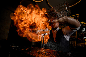 Close-up of a cocktail glass into which the bartender sharply pours the prepared drink
