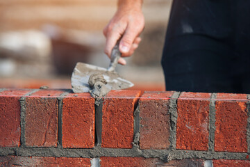 A skilled mason laying bricks with precision during construction in a sunny outdoor setting
