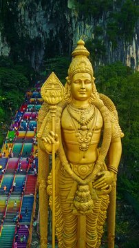 A large golden statue of Lord Murugan stands majestically at Batu Caves, Malaysia. Vertical shot. Aerial view