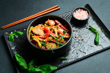 Udon pasta with chicken and ginger. In a black plate. Japanese cuisine. On a dark background, close-up.