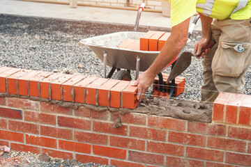 Bricklayer constructing a sturdy brick wall with precision at a building site during daylight hours