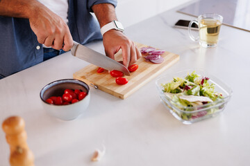 Partial shot of african american man cutting cherry tomatoes near salad in bowl and tea in kitchen