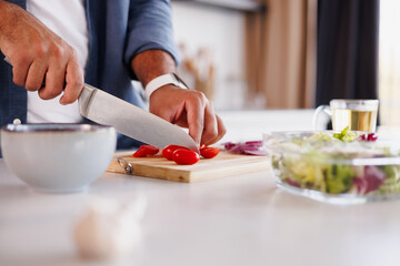 Partial shot of african american man cutting cherry tomatoes near blurred salad on table in kitchen