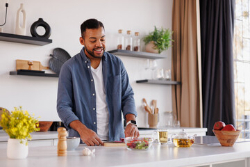 African american man cooking fresh salad near tea in modern kitchen