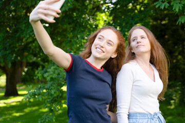 Two friends take a cheerful selfie together in a sunny park surrounded by lush green trees in the afternoon