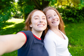 Naklejka premium Two smiling friends take a selfie together in a park on a sunny day surrounded by green trees and grass