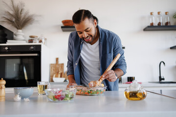 Smiling african american man cooking chicken legs near tea and fresh salad in kitchen at home