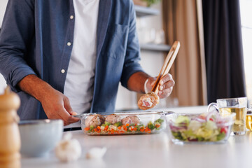 Partial view of african american man putting raw chicken legs in baking dish near tea and salad in kitchen